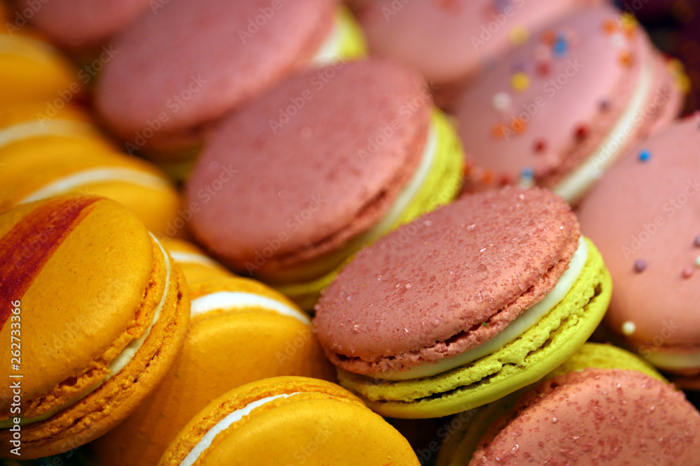 Macaroons in a row close up, colorful sweet background. Pink, yellow and orange almond cookies with filling, bright colours Macaroons in a row close up, colorful sweet background. Pink, yellow and orange almond cookies with filling, bright colours
