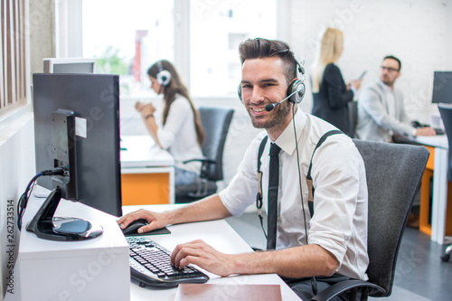 Smiling friendly customer support operator with headset working on computer in call center © Bojan