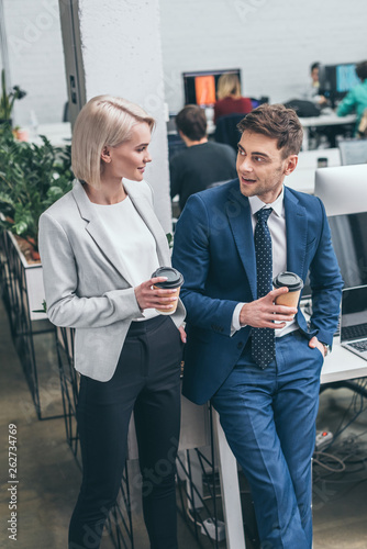 pretty businesswoman and handsome businessman holding paper cups and talking in offce photo