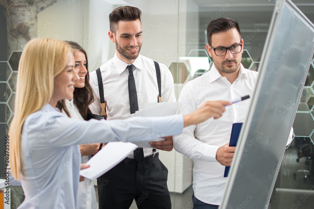 Young businesswoman explaining financial graphs on flipchart to her partners in the meeting office