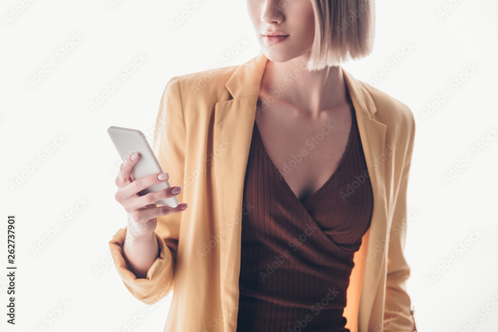 partial view of fashionable woman holding smartphone on grey partial view of fashionable woman holding smartphone on grey