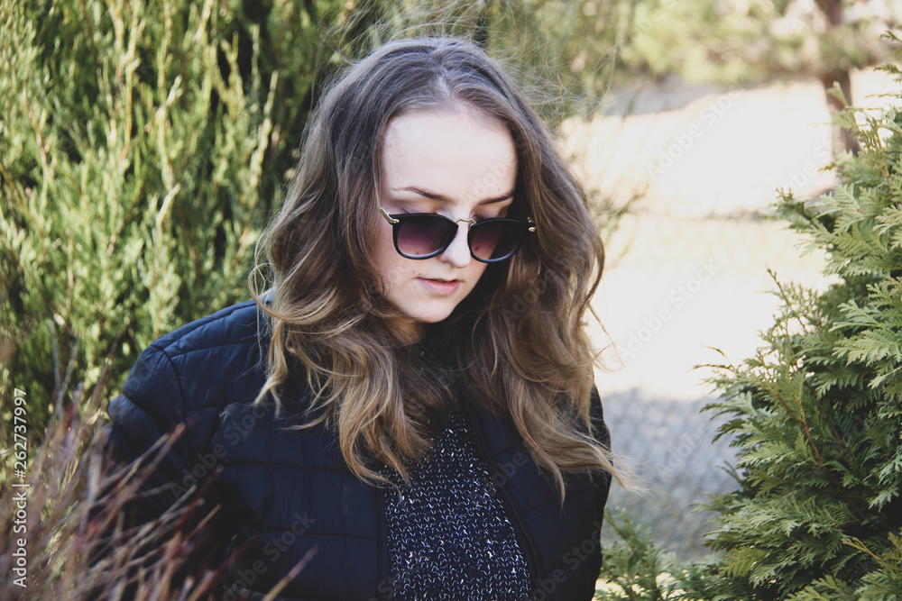 Woman tourist enjoying fresh air while resting after strolling in forest in sunny spring day, female in trendy sunglasses admires nature while standing near tall trees in the park during fall weekend Woman tourist enjoying fresh air while resting after strolling in forest in sunny spring day, female in trendy sunglasses admires nature while standing near tall trees in the park during fall weekend