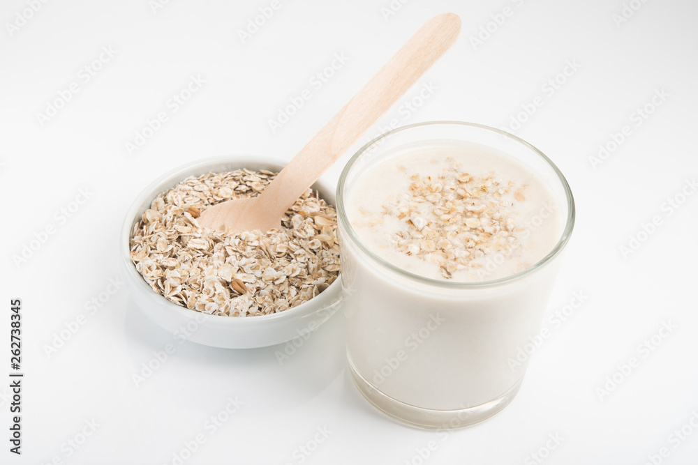Glass of oat milk and grains in white bowl Glass of oat milk and grains in white bowl