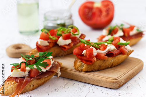 Italian appetizer - bruschetta with tomatoes, chili, sausage and cheese on a wooden board
