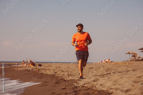 Young man jogging on the beach by the sea