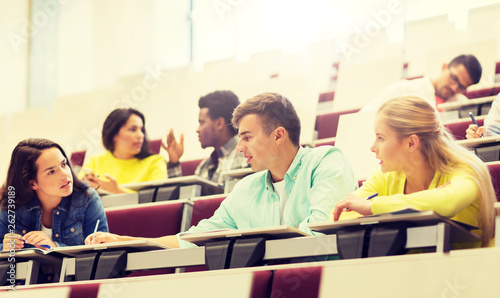 education, high school, university, learning and people concept - group of international students with notebooks writing in lecture hall