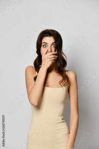 Young beautiful woman with eyes wide open covers her mouth with hand like she is scared much, very surprised or keeps a secret