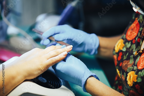 Manicurist master make manicure in blue gloves with nail file. Woman getting nail manicure