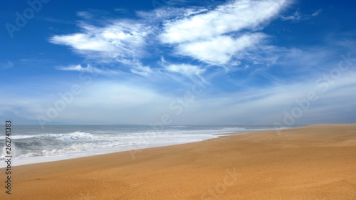 Wide sandy deserted beach by the sea with waves under a blue sky