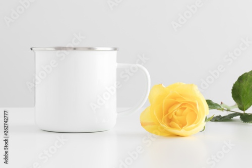 Fototapeta Naklejka Na Ścianę i Meble -  Enamel mug mockup with a yellow rose on a white table.