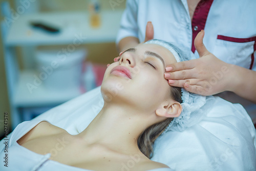 people, beauty, lifestyle and relaxation concept - beautiful young woman lying with closed eyes and having face and head massage at spa