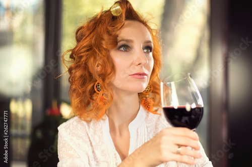 Portrait of a redhead girl in hair curlers with a glass of red wine