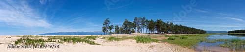 Beautiful lakeshore panorama of white sand and pine forest on mountains background