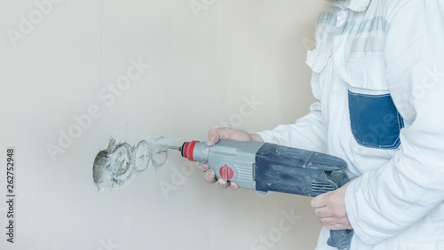 A man drills a wall with a perforator. A man works with construction tools.