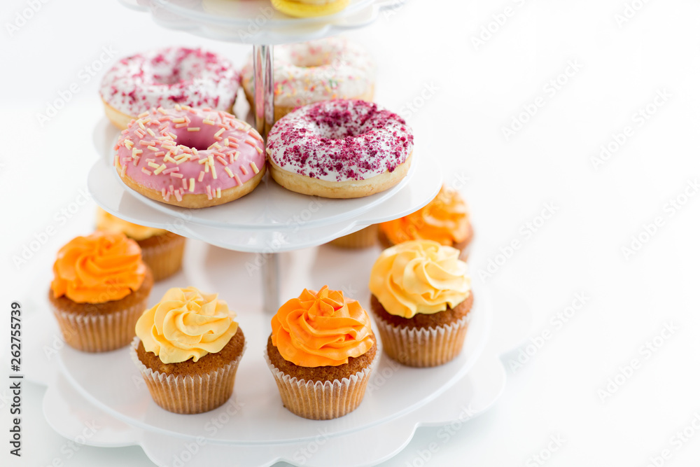 fast food and sweets concept - glazed donuts and cupcakes with buttercream frosting on stand over white background fast food and sweets concept - glazed donuts and cupcakes with buttercream frosting on stand over white background