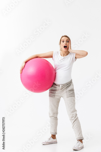 Beautiful shocked young pregnant yoga fitness woman posing isolated over white wall background make exercises with ball.