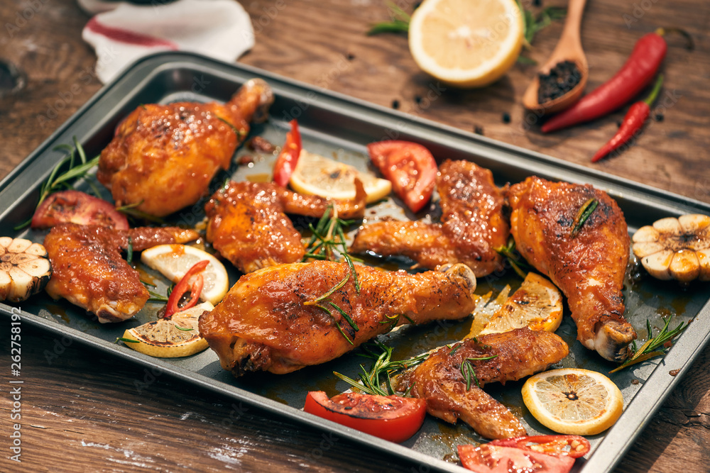 Baked chicken drumstick and wings on baking tray over dark wooden background.