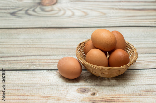  Raw chicken eggs in a wicker basket on a wooden background