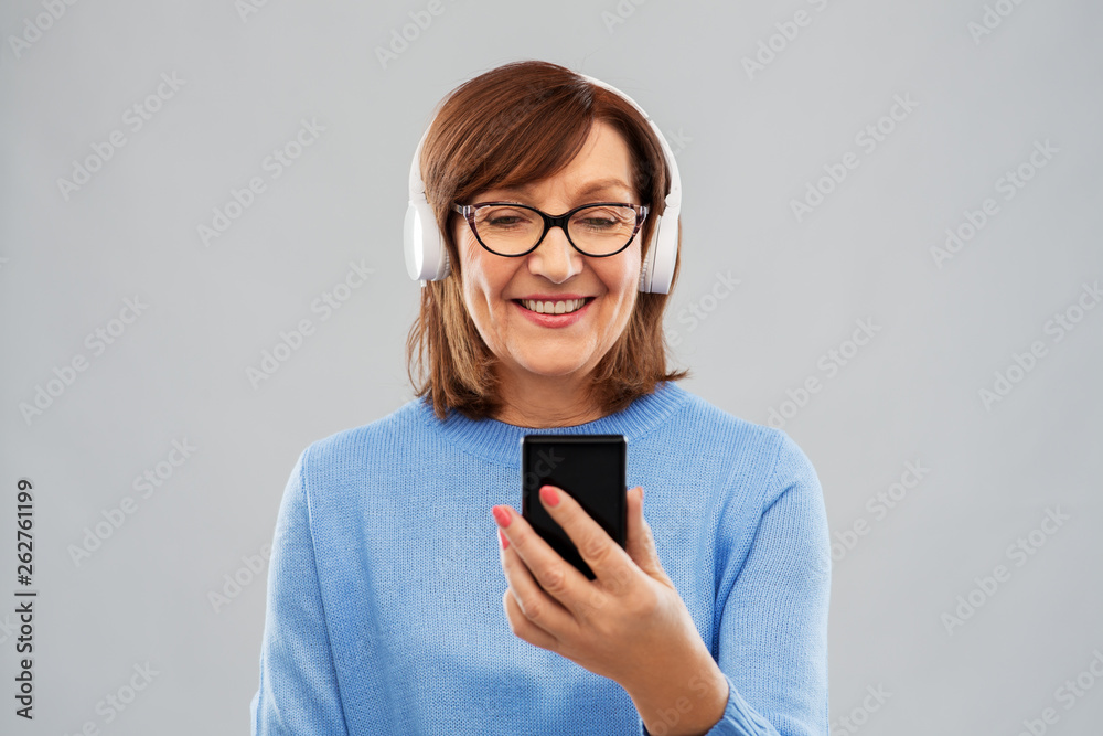 technology and old people concept - smiling senior woman in glasses and headphones listening music on smartphone over grey background technology and old people concept - smiling senior woman in glasses and headphones listening music on smartphone over grey background