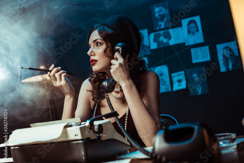 Attractive woman with mouthpiece talking on telephone in dark office