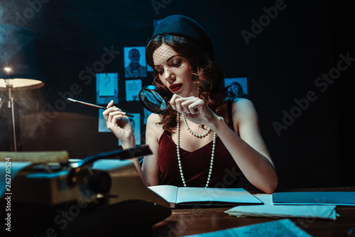 Attractive woman in fascinator hat holding mouthpiece and magnifier in dark office