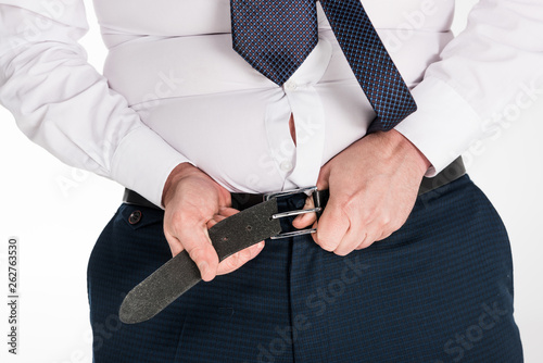 partial view of overweight man in formal wear putting on tight pants isolated on white