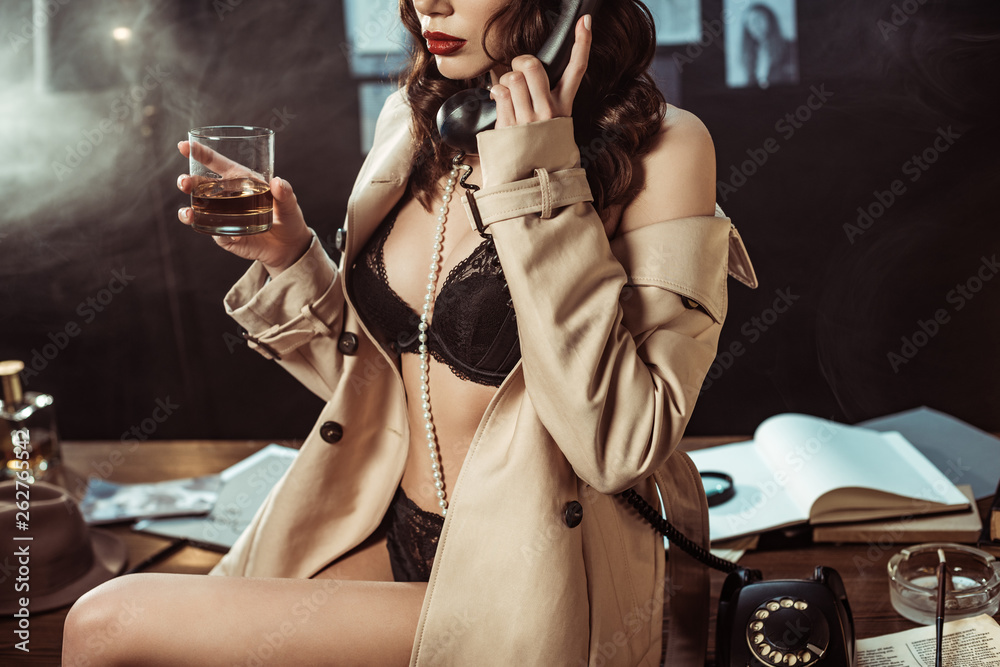 Partial view of sexy woman in black lingerie and trench coat holding glass  of cognac while talking on telephone Stock Photo | Adobe Stock