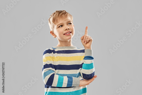 childhood, expressions and people concept - little boy in striped pullover pointing finger up over grey background