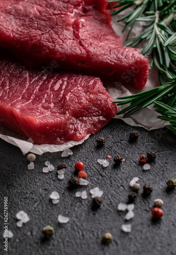 raw beef steak with rosemary branches on parchment paper with pepper and salt photo