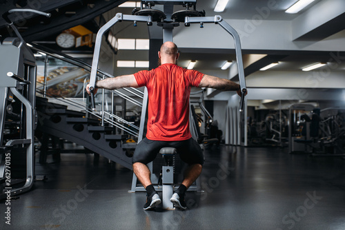 Muscular athlete on exercise machine, back view