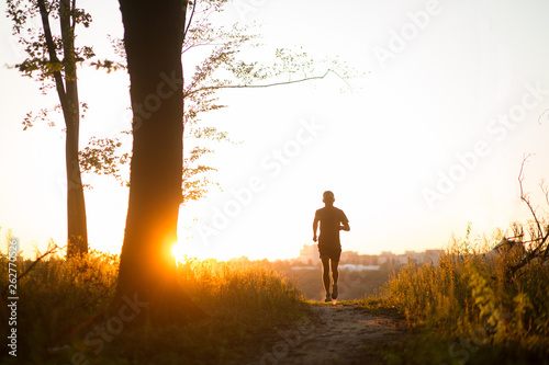 Sport running man in cross country trail run on sunset