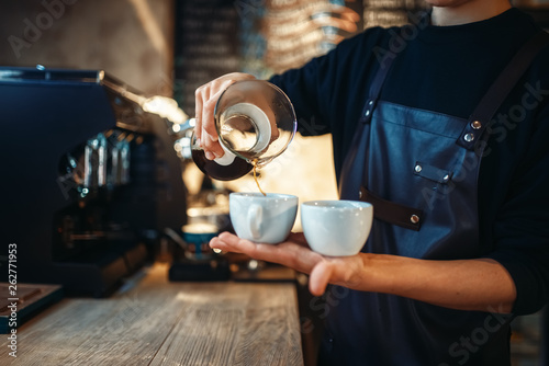 Young male barista holds two cups of fresh coffee