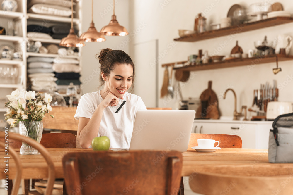 Beautiful young student girl with apple indoors using laptop computer holding credit card. Beautiful young student girl with apple indoors using laptop computer holding credit card.