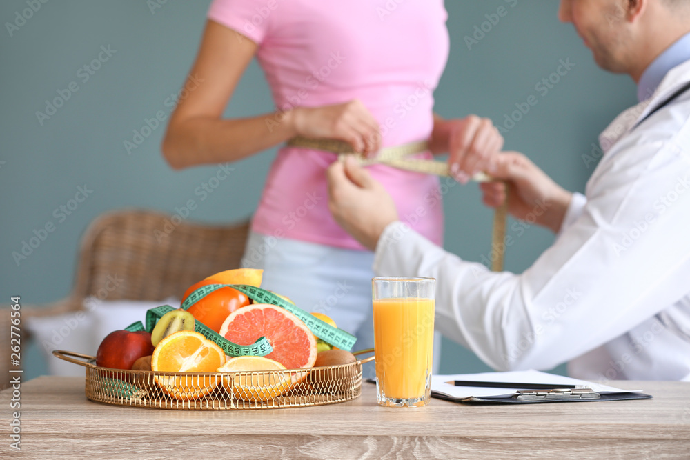 Assortment of fresh fruits with measuring tape and glass of juice on table of nutritionist