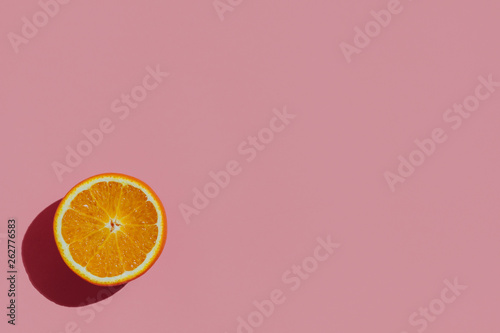 Fresh cutted orange on a pastel pink background at the left corner of the table with space for text