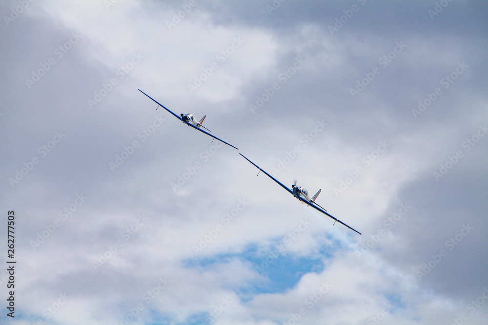 Low angle view of two aerobatic planes performing maneuvers against a cloudy sky. Precision and skill concept. Low angle view of two aerobatic planes performing maneuvers against a cloudy sky. Precision and skill concept.