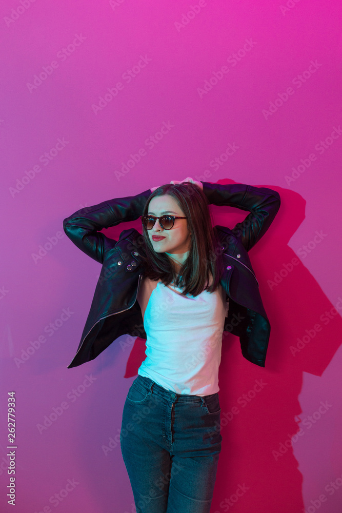Fashioned girl in leather jacket in dark glasses in pink anf blue neon lights background. Fashioned girl in leather jacket in dark glasses in pink anf blue neon lights background.