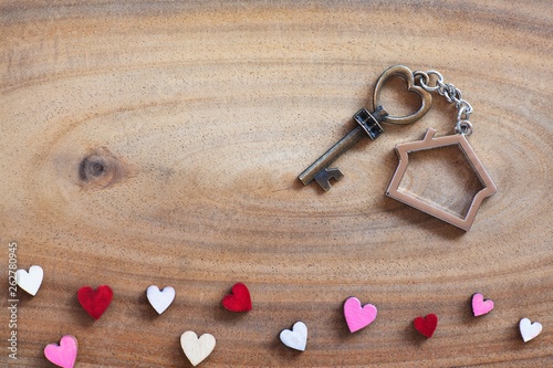 House key in heart shape with home keyring on old wood background decorated with mini heart