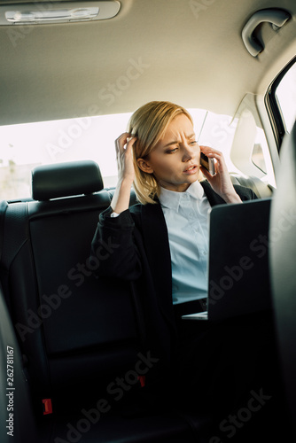 confused blonde woman talking on smartphone near laptop in car © LIGHTFIELD STUDIOS