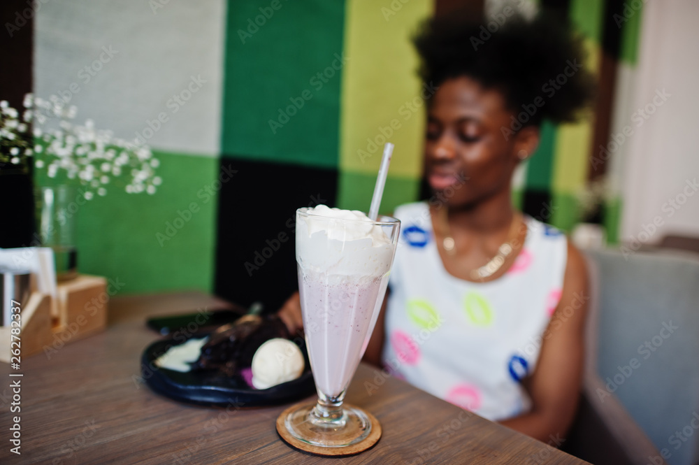 Close up milkshake coctail against cheerful african american young woman in summer dress at cafe.