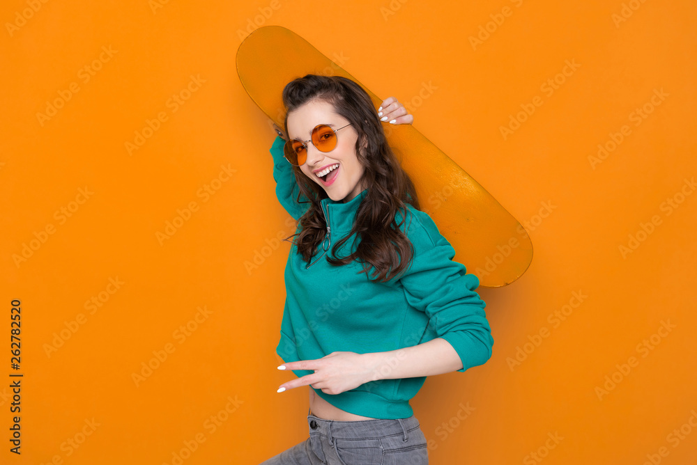 Waist up of stylish Caucasian girl posing for camera with skateboard