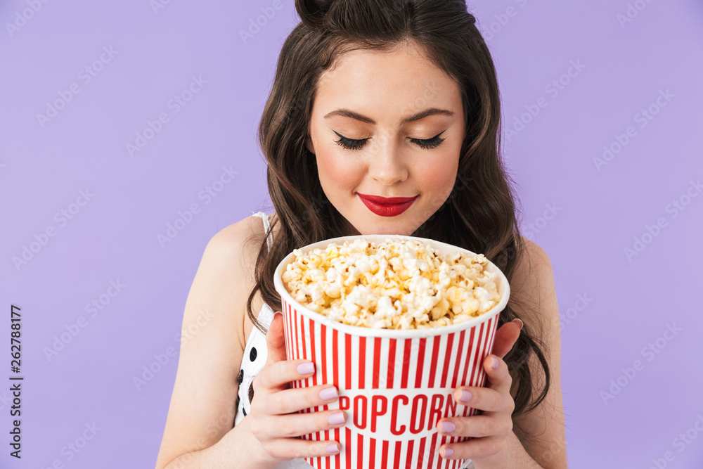 Portrait of caucasian pin-up woman 20s in retro polka dot dress holding bucket with popcorn while watching movie