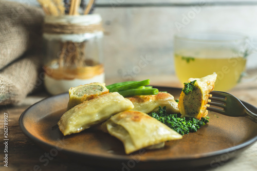 traditional German cuisine, delicious, baked Maultaschen with spinach sauce and green legumes, next to it stands a glass of hot broth of beef