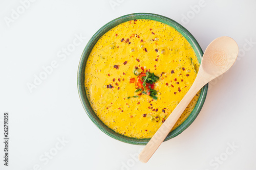 Hot creamy delicious soup with greenery and vegetables, wooden spoon on bowl, isolated over white background. Coconut curry soup. Fresh disn. Healthy eating concept photo