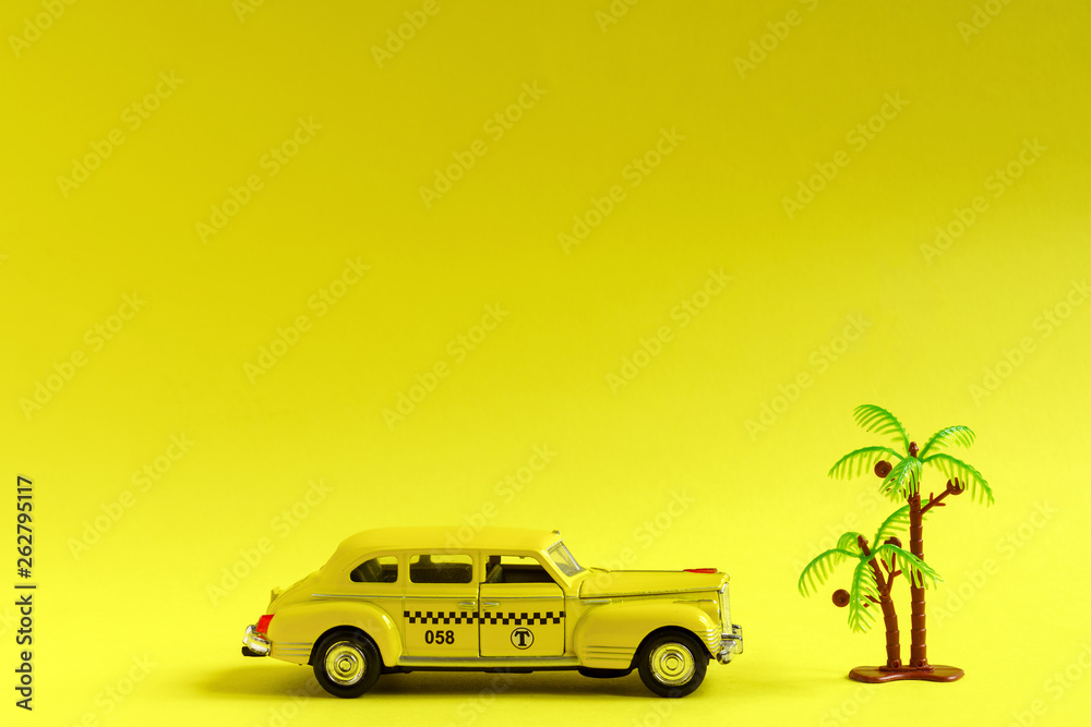 Old retro yellow toy car taxi and toy palm on yellow background with copy space. Travel concept