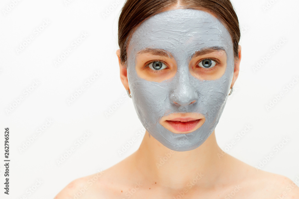 Portrait of young lady is looking at camera with joy while touching her face with clay mask while using procedures. white background. Beauty concept Portrait of young lady is looking at camera with joy while touching her face with clay mask while using procedures. white background. Beauty concept