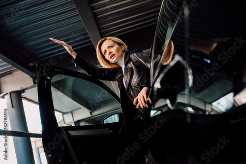 low angle view of surprised blonde girl near black car with open door © LIGHTFIELD STUDIOS
