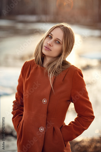 beautiful woman with blonde hair in red coat walking on a sunny day on background of awesome landscape
