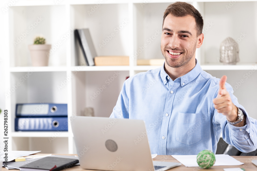 cheerful businessman pointing with finger and looking at camera near laptop cheerful businessman pointing with finger and looking at camera near laptop
