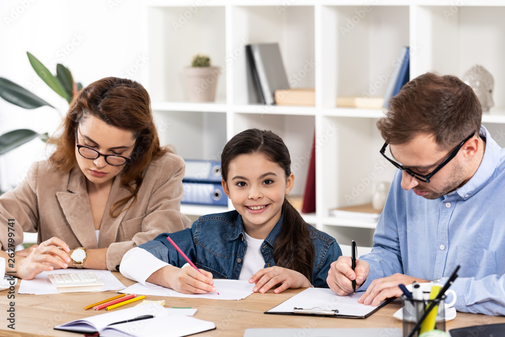 cute child drawing near parents in glasses working in office cute child drawing near parents in glasses working in office